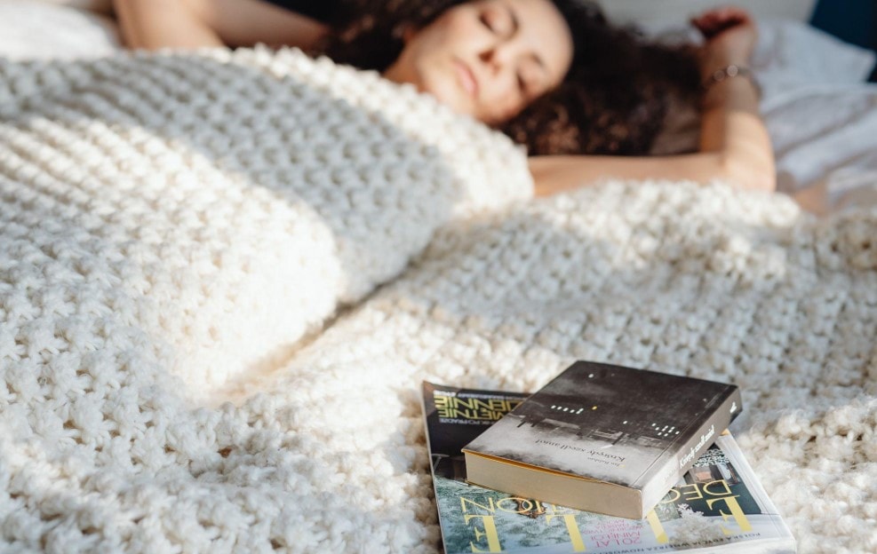 woman sleeping with a knitted blanket beside books