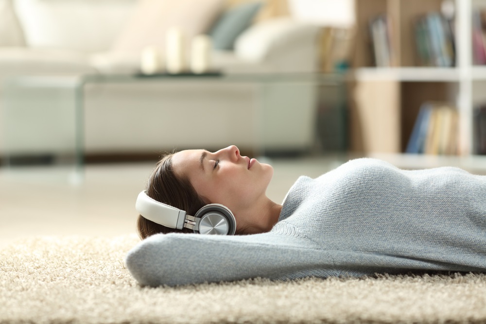 portrait of a relaxed woman listening to music with headphones lying on a carpet at home