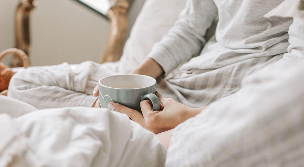 A person relaxing in bed with a blanket and a cup of coffee