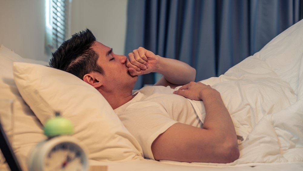 Man lying on his back in bed covering his mouth