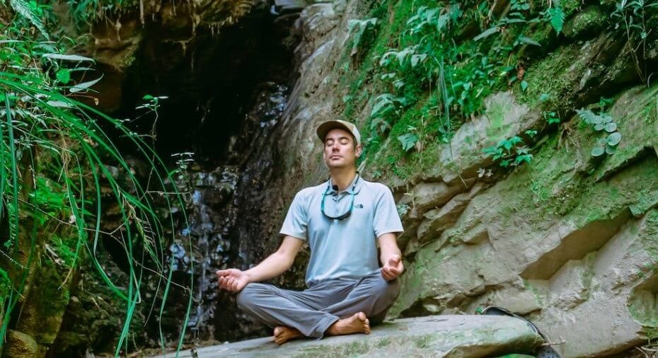 Man meditating on a rock by a waterfall - Quiet Nature