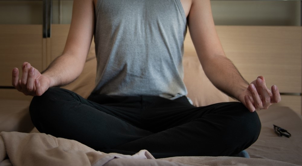 Man sitting in yoga pose on bed