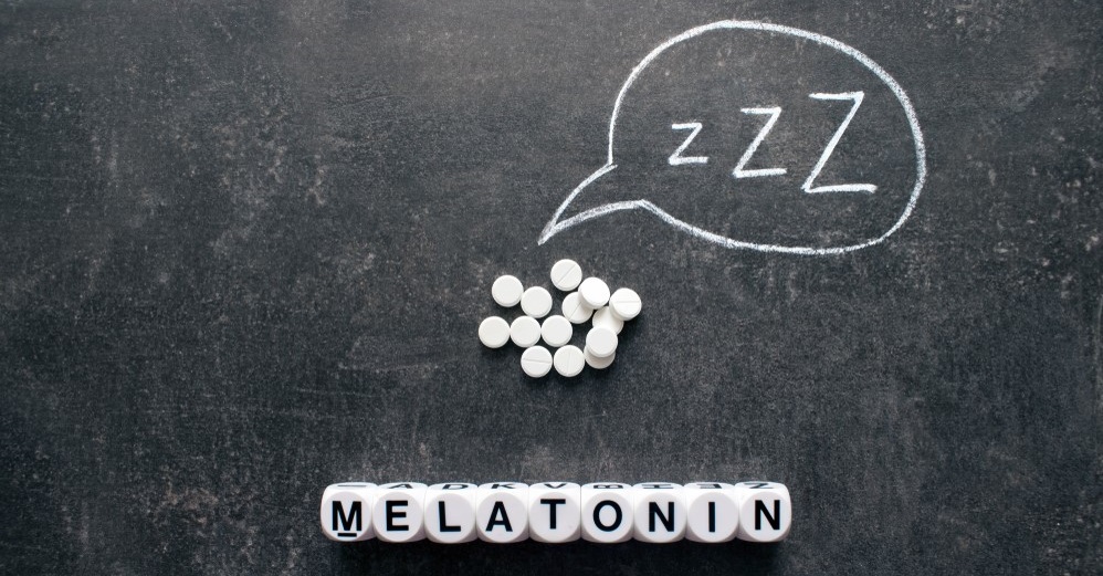 Melatonin spelled out in white cubes below melatonin pills on chalkboard
