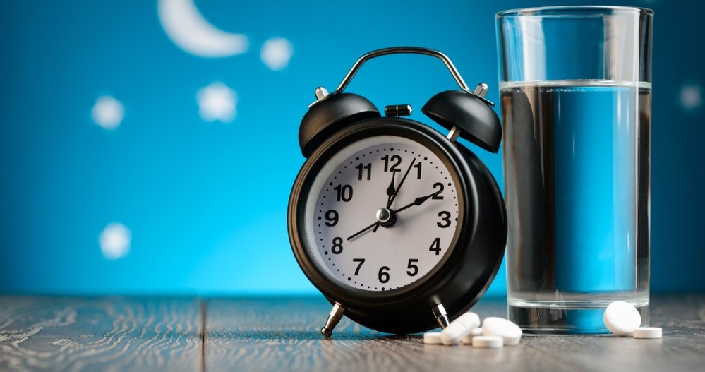 Sleeping pills beside glass of water and alarm clock