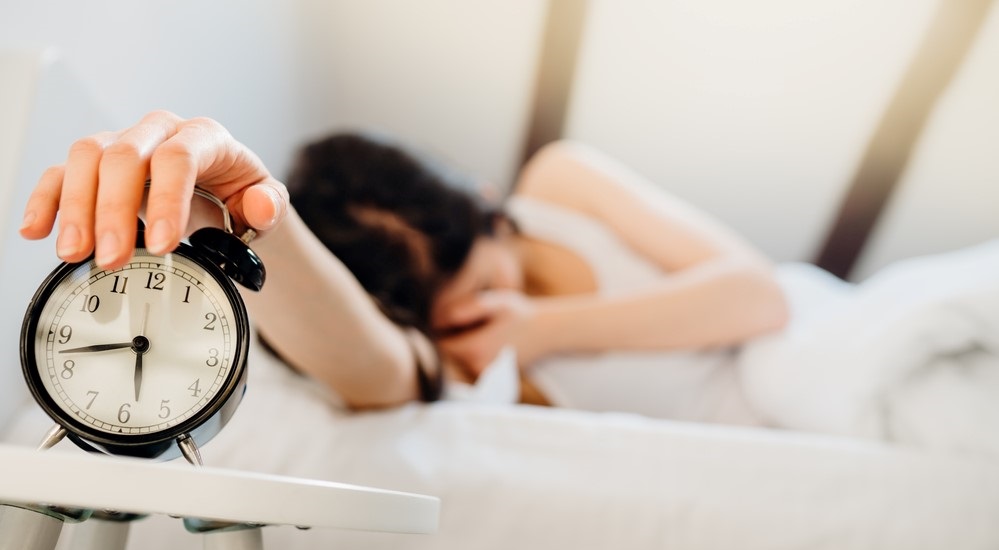 Tired young woman reaching over to shut off alarm clock