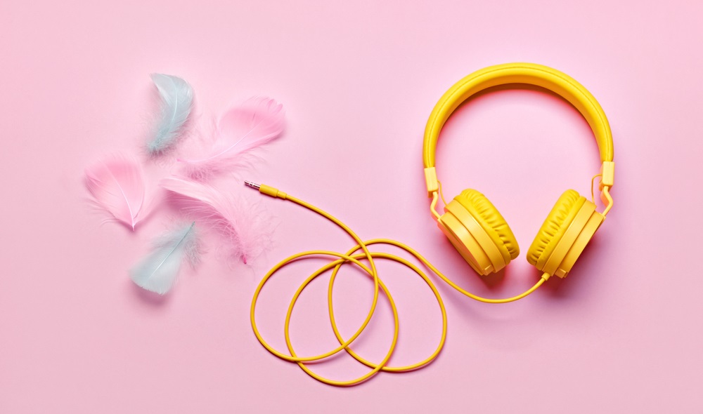 Yellow headphones and soft feathers on pink background