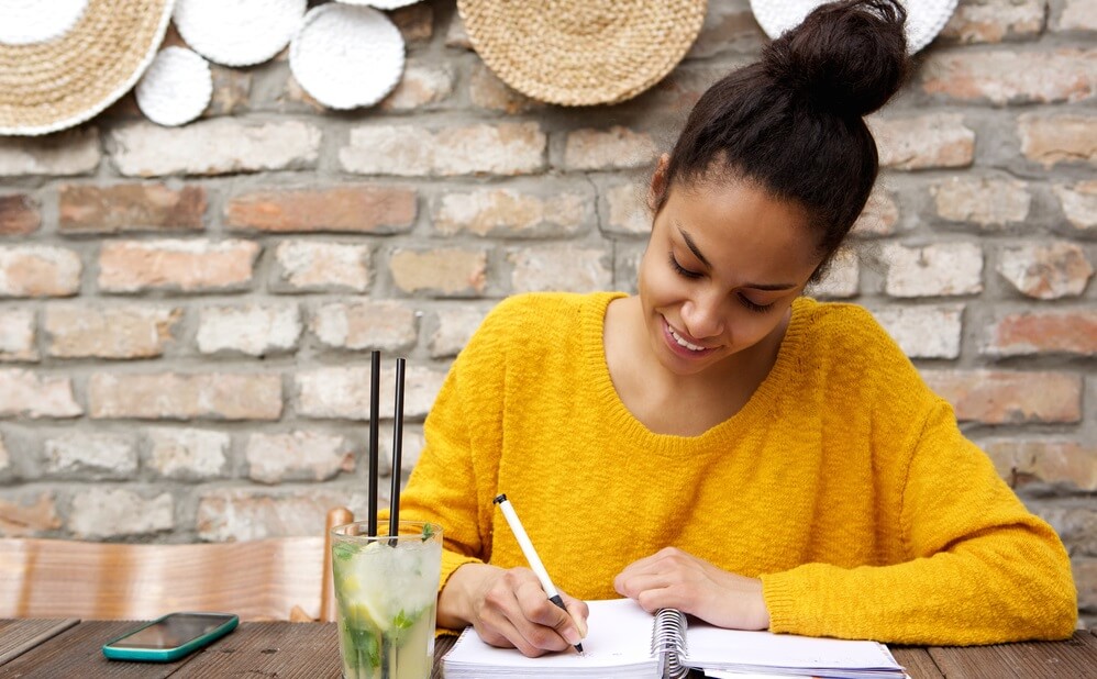 beautiful young black woman sitting at cafe and writing notes