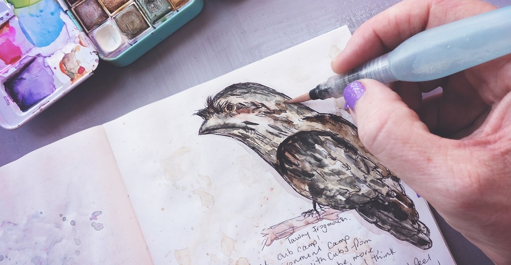 paintbrush water brush pen and watercolor palette painting Tawny Frogmouth bird in an art journal sketch book