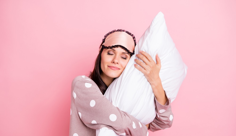 sleepy young woman sleepwear lying embracing pillow closed eyes isolated pink color background