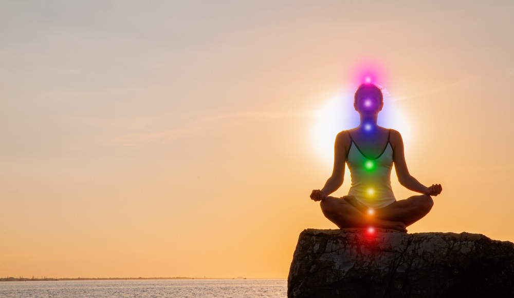 woman is meditating with glowing seven chakras on stone at sunset